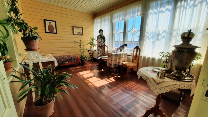 Veranda ar skatu uz upi, pie loga stāv Aspazijas tēls