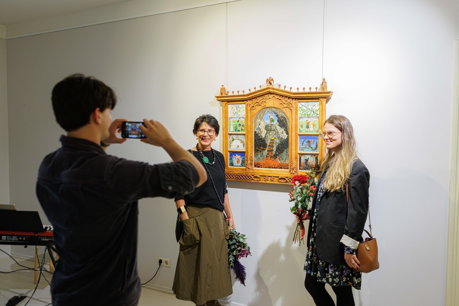 Vīrietis bildē divas dāmas pie mākslas darba