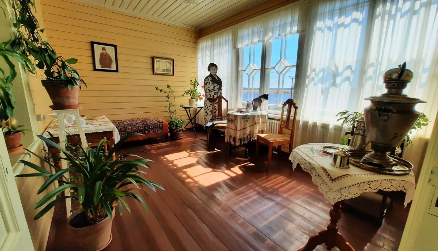 Veranda ar skatu uz upi, pie loga stāv Aspazijas tēls