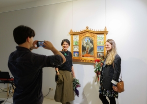 Vīrietis bildē divas dāmas pie mākslas darba